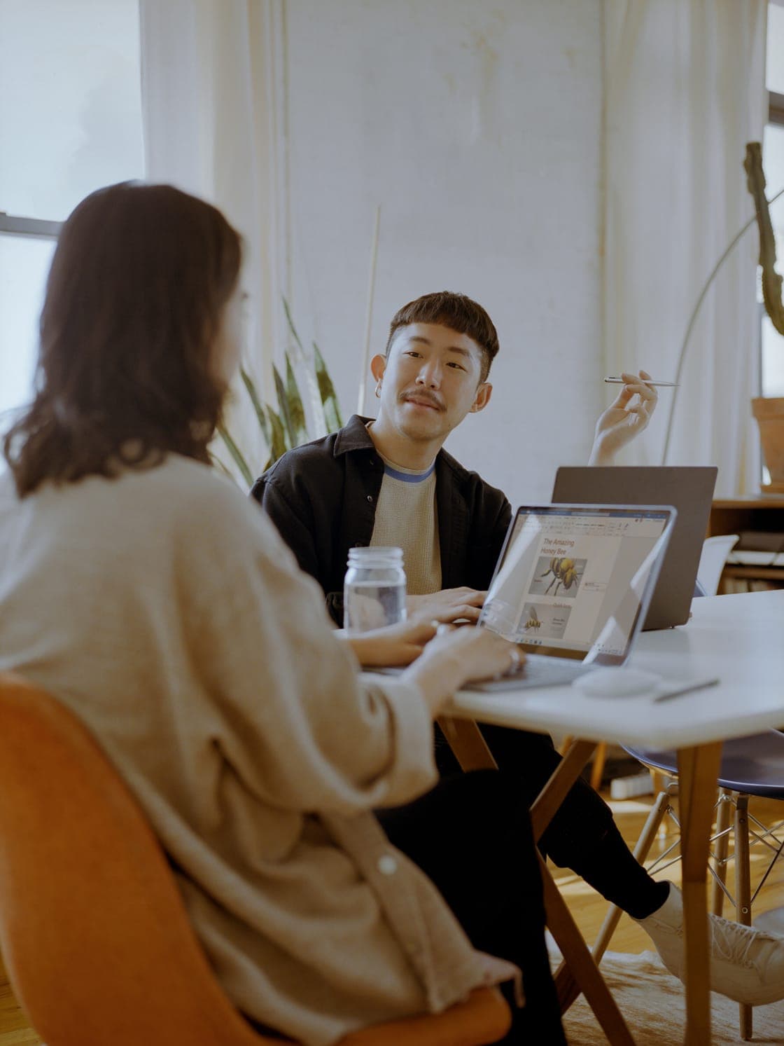 A woman and a smiling man talking over a laptop at a white table