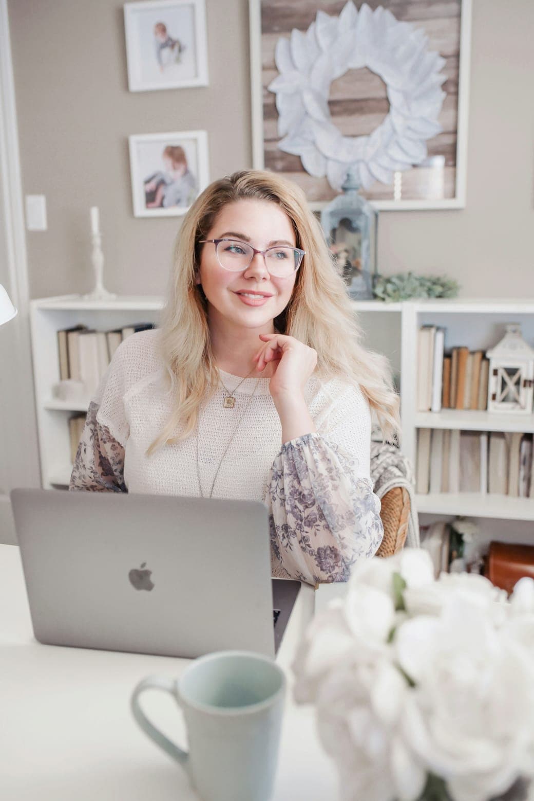 A smiling woman with glasses working on a laptop in a bright room