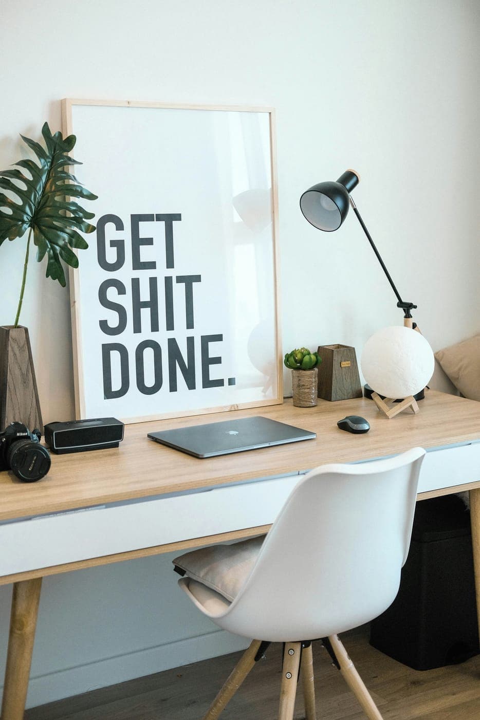 A tidy wooden desk with a laptop, a lamp, a plant and a framed motivational poster