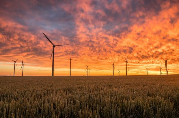 Wind turbines under a fiery orange sky over a wheat field