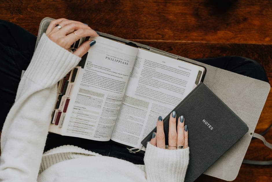 A person holding an open book and a notes journal on their lap