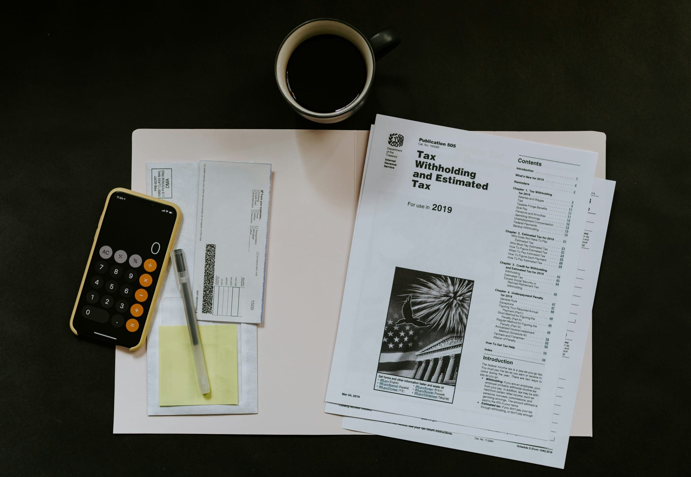 A calculator, a phone, tax forms and a cup of coffee on a dark desk