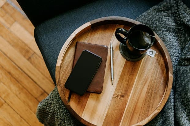 A wooden tray with a phone, a pen and a black cup