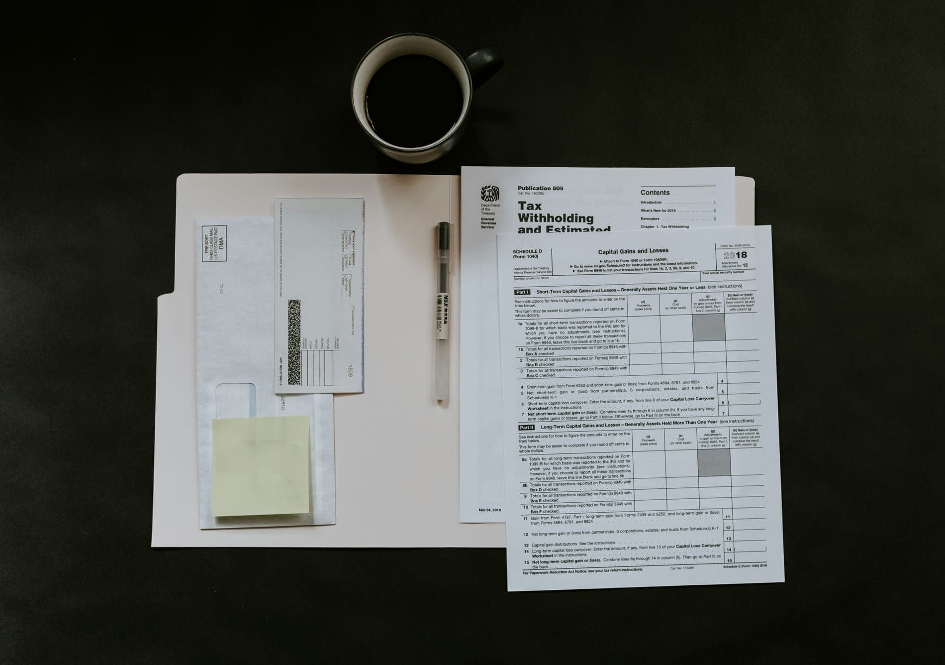 Tax withholding forms, notes and a cup of coffee on a dark desk