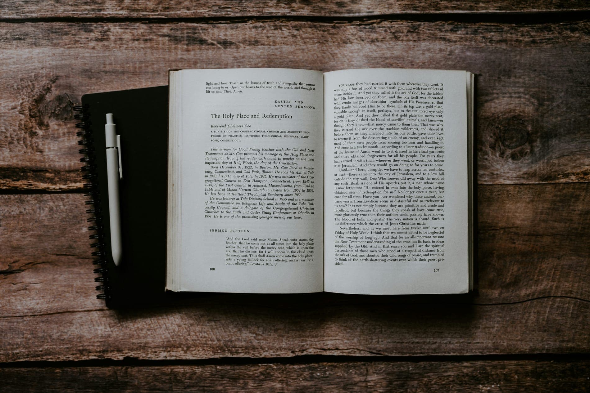 An open book and a notebook with a pen on a rustic wooden table