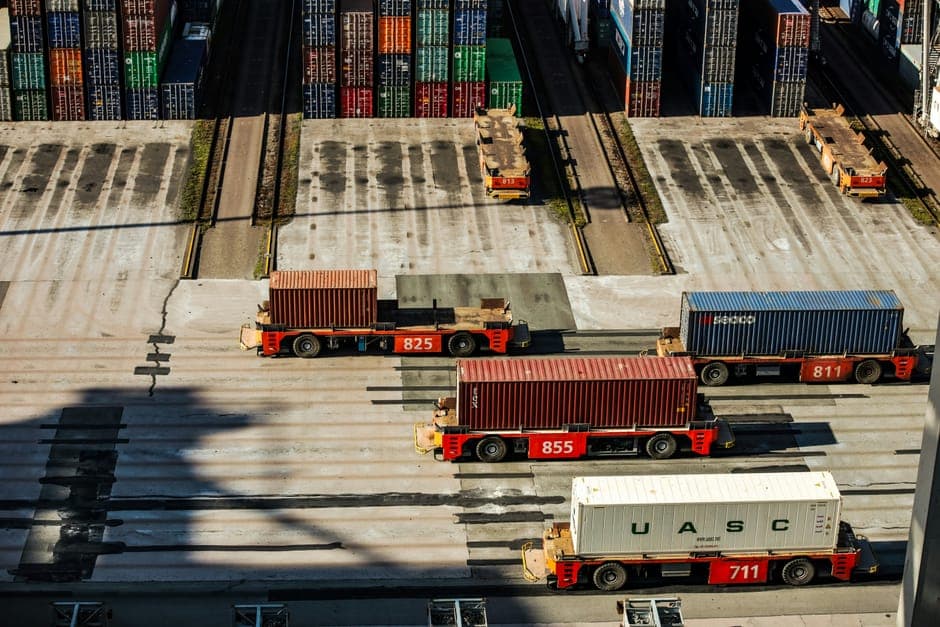 Container trucks driving across a terminal yard in strong sunlight