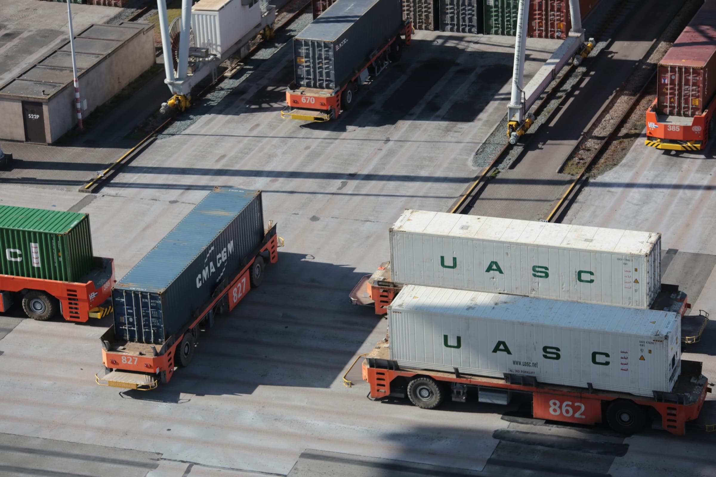 Two automated carriers moving white shipping containers at a port terminal