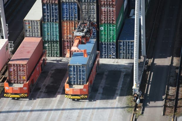 A carrier loading a blue container beside tall stacks of containers