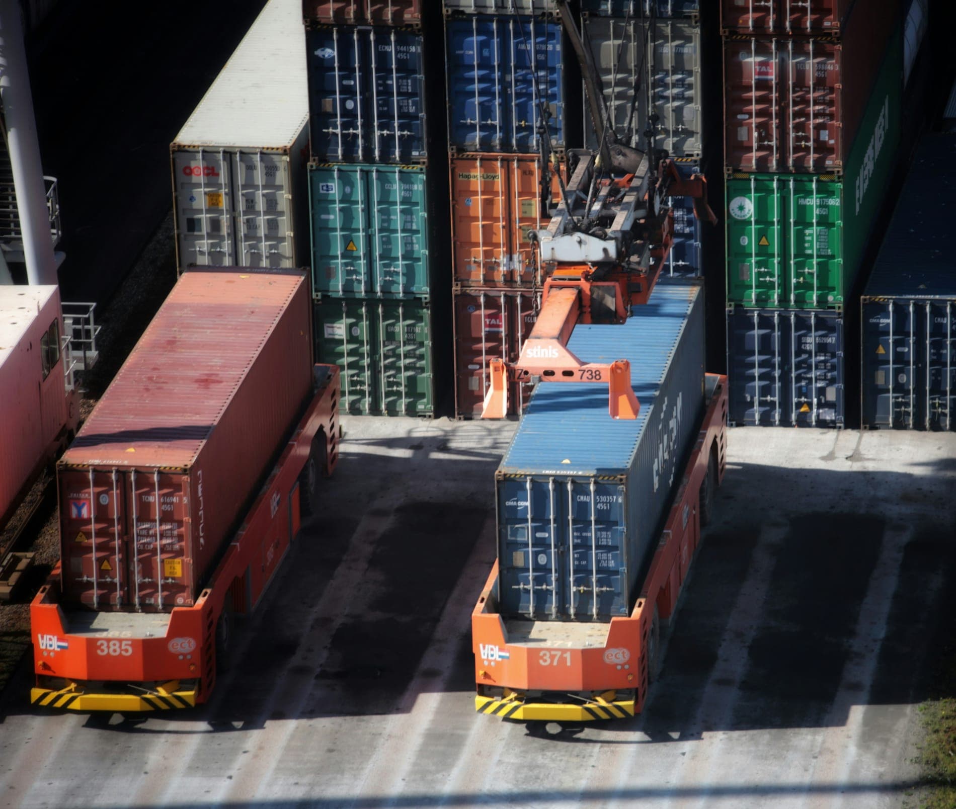 Orange carriers moving containers in front of container stacks