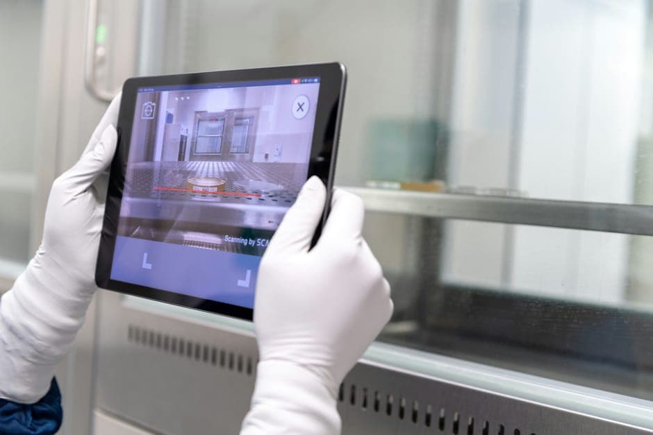 Gloved hands holding a tablet in front of a stainless steel cabinet