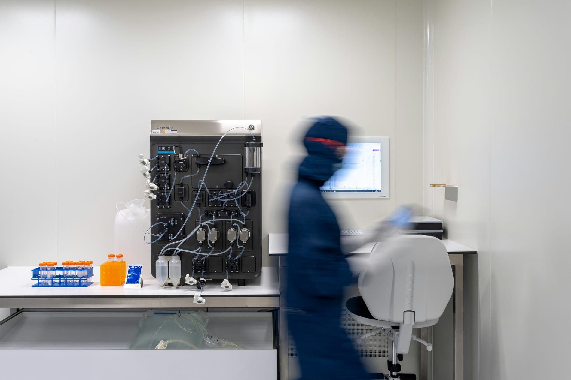 A blurred lab worker walking past lab equipment in a cleanroom