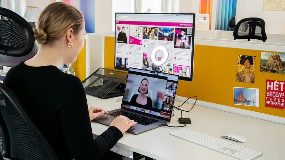 A woman working at a desk with a laptop video call and a large monitor
