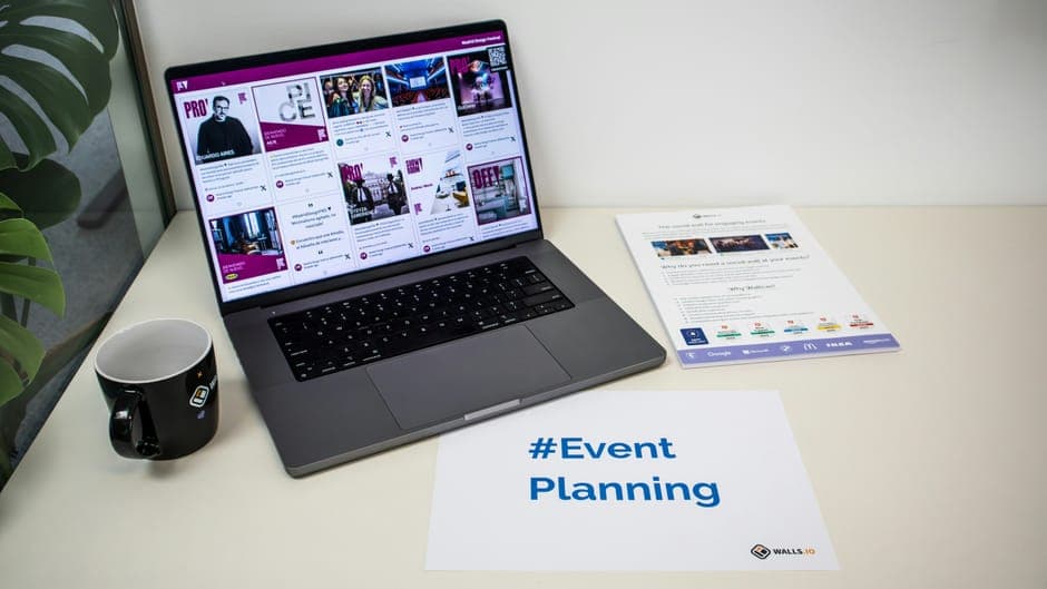 A laptop on a desk with a coffee mug and an event planning sign