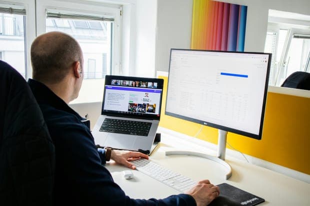 A man at a desk with a laptop and a large monitor