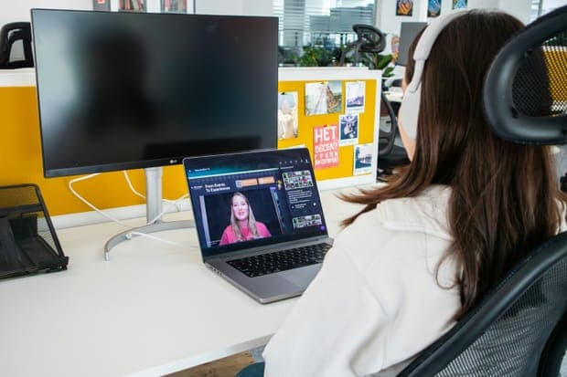 A woman with headphones watching a video call on a laptop