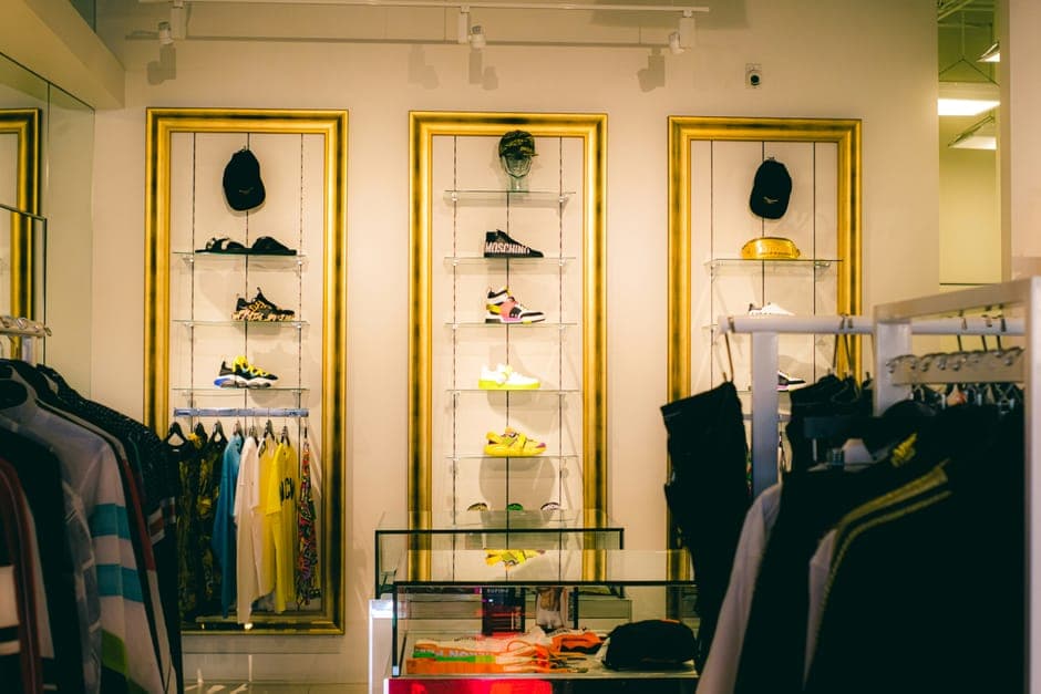 A shop display of sneakers and caps in gold frames above racks of clothes