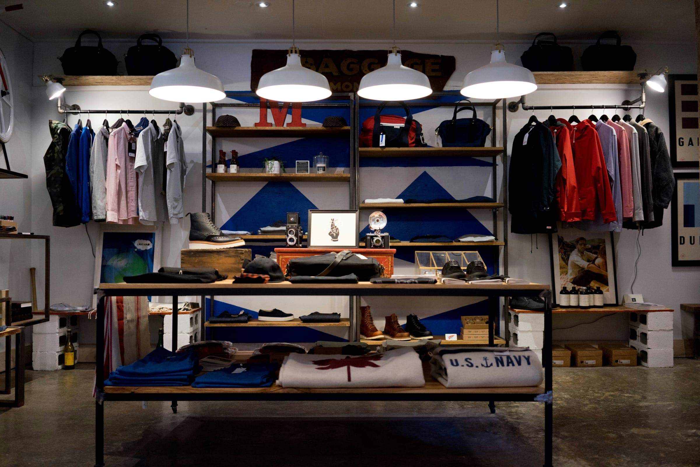 A boutique with clothes on shelves and tables under white pendant lamps