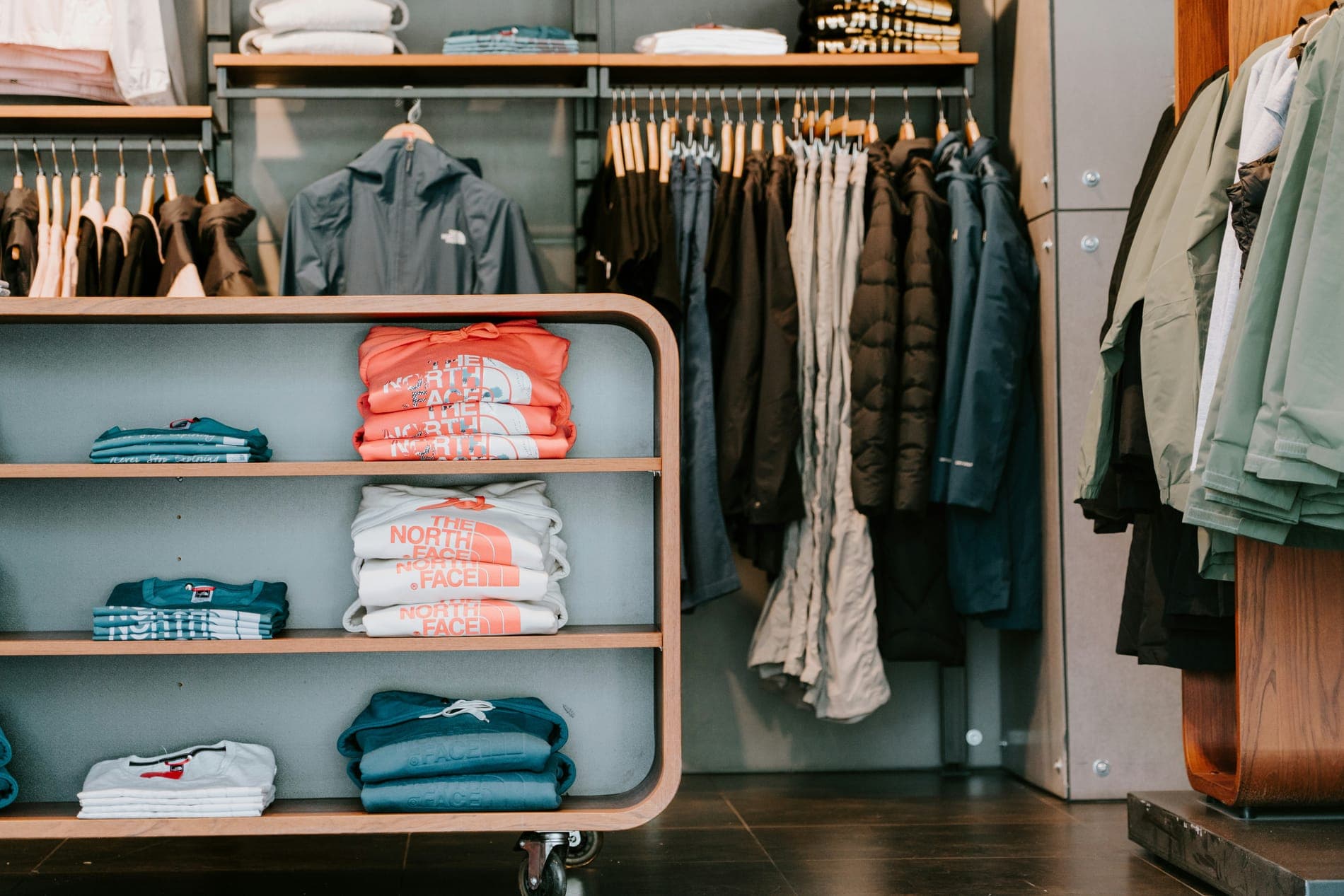 A boutique with folded T-shirts on a rounded shelf beside a rail of jackets