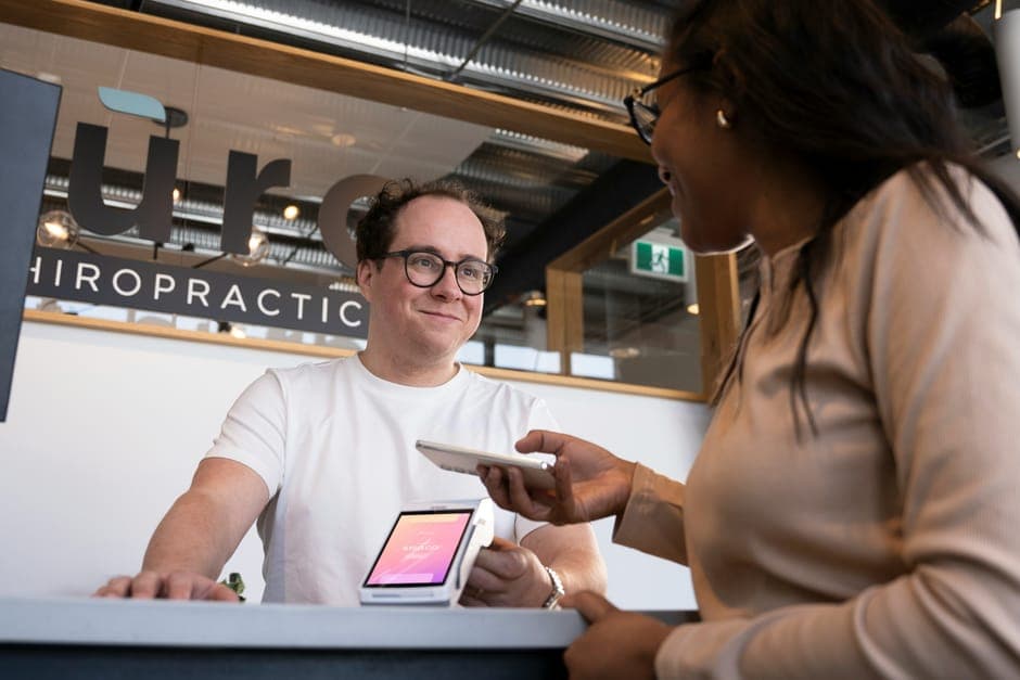A smiling man in a white T-shirt taking a contactless payment from a customer