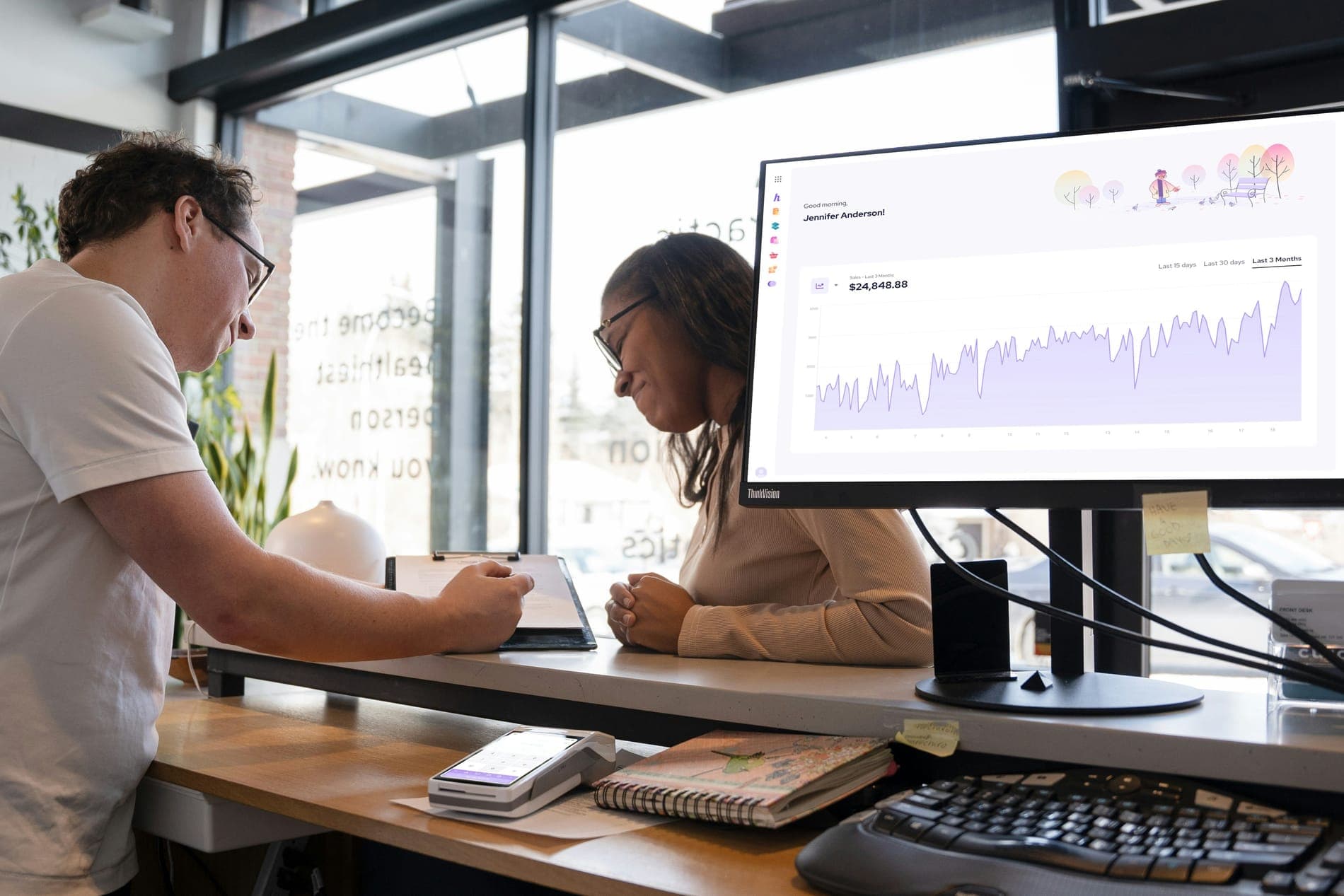 Two colleagues at a desk reviewing a sales chart on a monitor