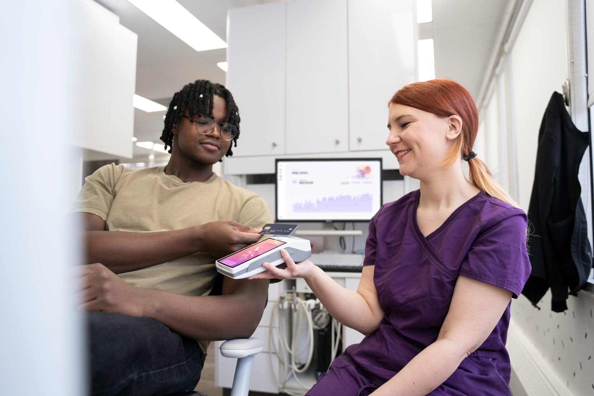 A smiling nurse in purple scrubs taking a contactless payment from a patient