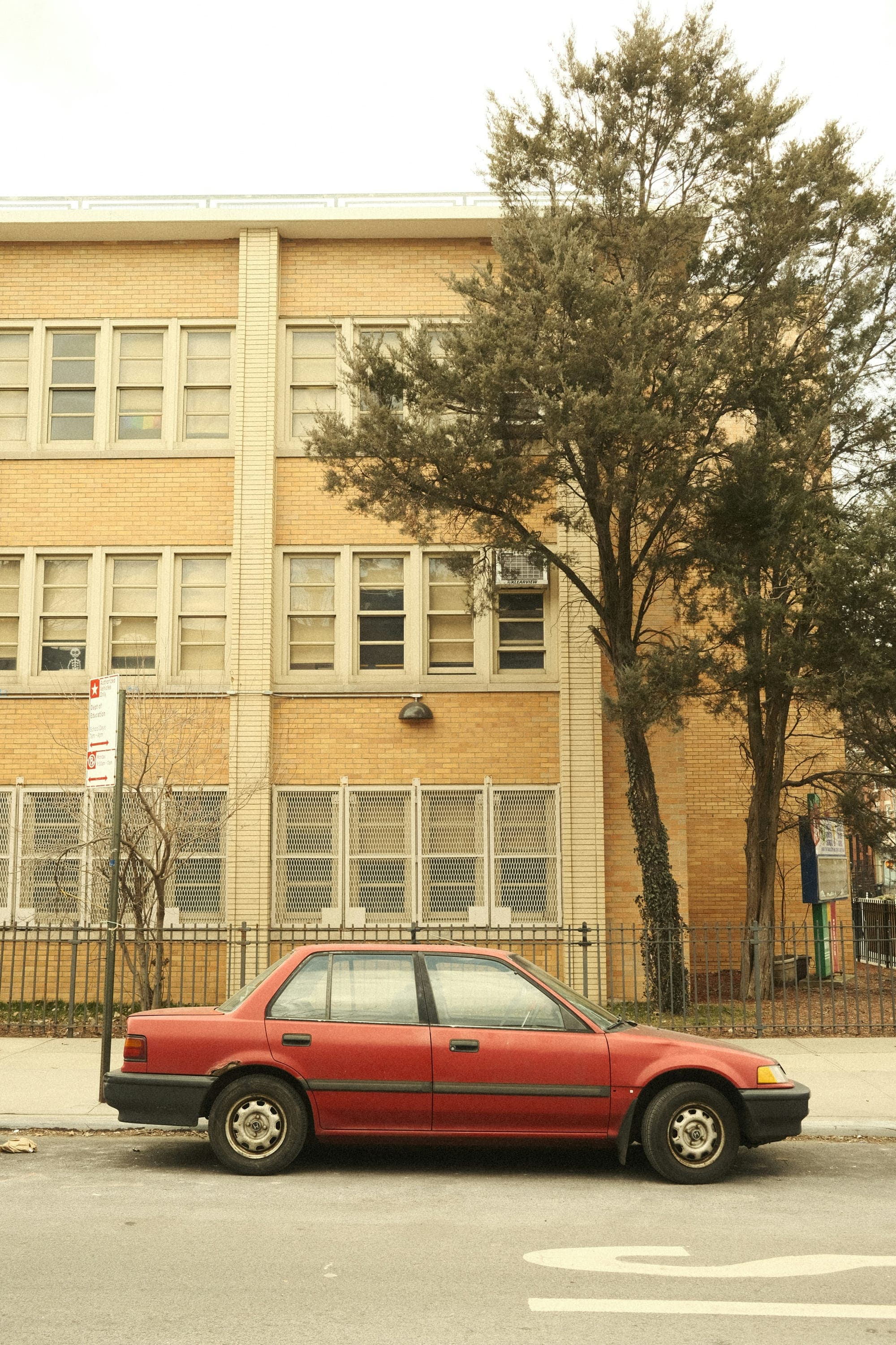 A tan brick building and a red car parked on a street