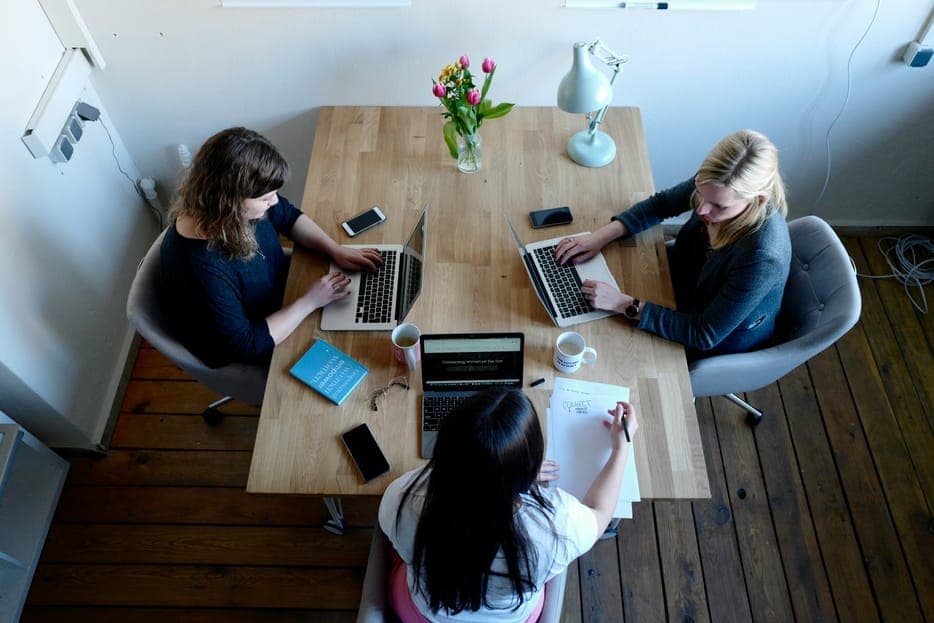 Three women working on laptops around a wooden table seen from above