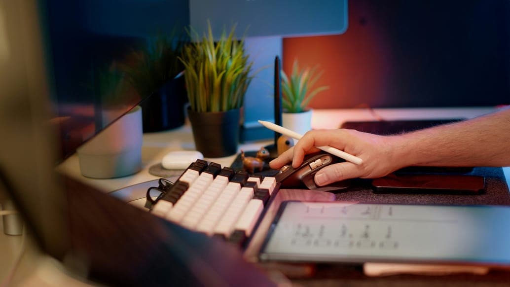A hand typing on a keyboard with a tablet and plants nearby