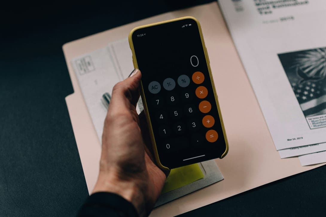A hand holding a phone with a calculator over loose papers