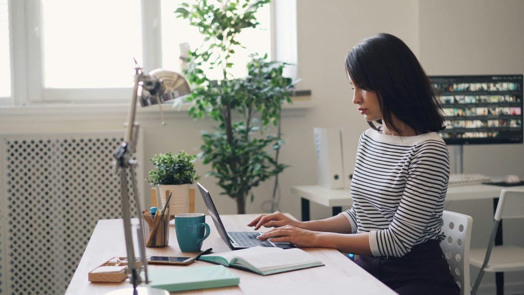 A woman in a striped top working at a laptop in a bright home office