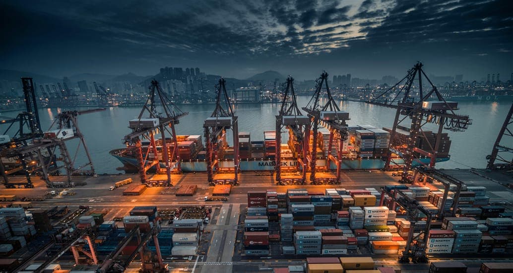 A container port at dusk with cranes and lit container stacks
