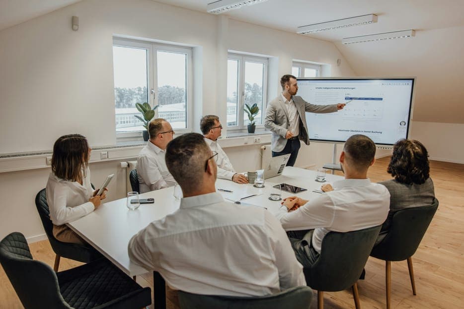 A man presenting on a wall screen to colleagues around a meeting table