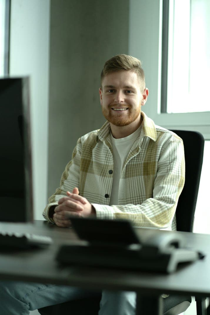 A smiling man in a light jacket sitting at a desk
