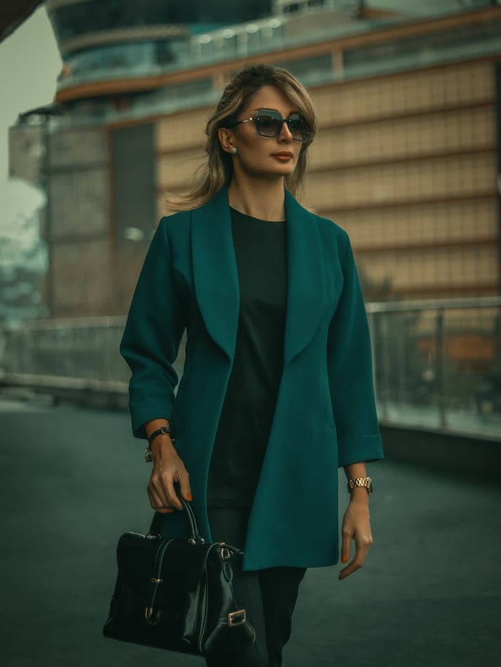 A woman in a teal coat holding a black handbag on a rooftop