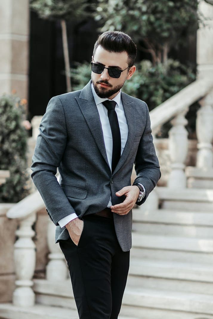 A man in sunglasses and a grey blazer standing by stone stairs